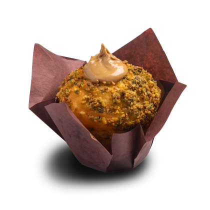 Muffin obalený drceným pistáciemi, s karamelovou polevou navrch, v hnědém tulipánovém košíčku.