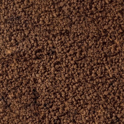Detailní záběr na drobivou hnědou hlínu nebo kávovou sedlinu s hrubou, zrnitou texturou.