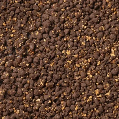 Detail drobivé tmavě hnědé směsi s kousky ořechů, připomínající čokoládový crumble.